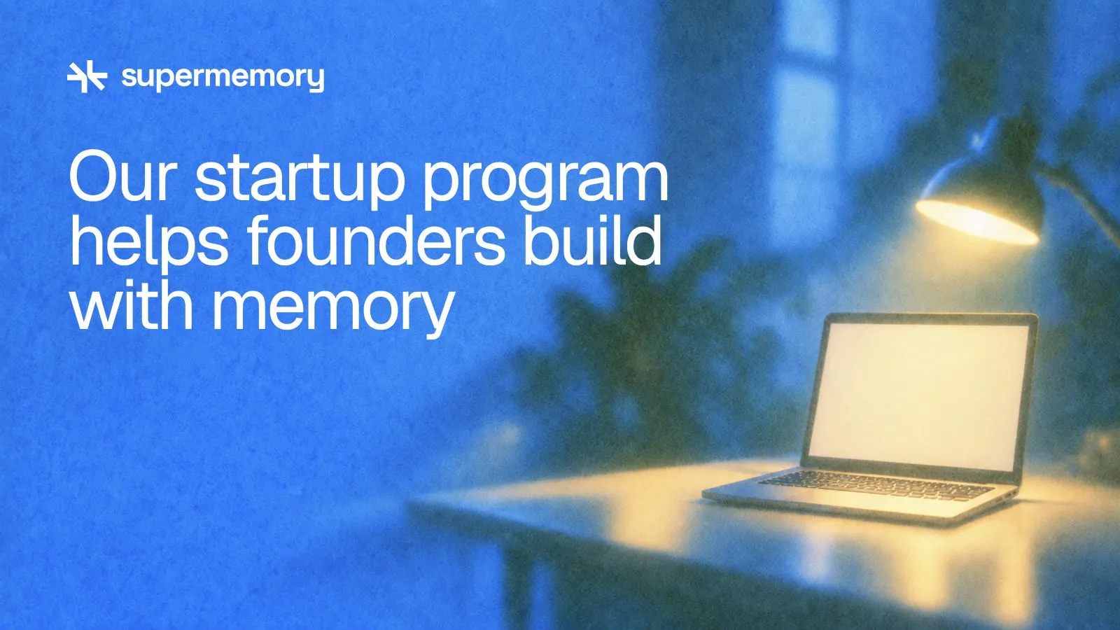 Supermemory header reading "Our startup program helps founders build with memory" — The laptop sits under the lamp and faces the person seated at the desk
